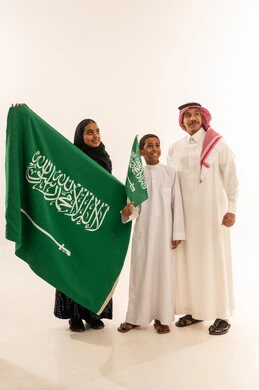 عائلة سعودية بالزي التقليدي تحمل العلم الوطني