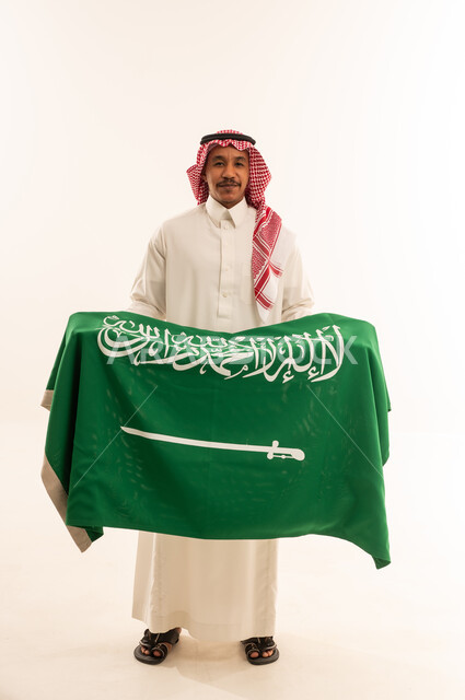 رجل سعودي بالزي التقليدي يحمل علم المملكة