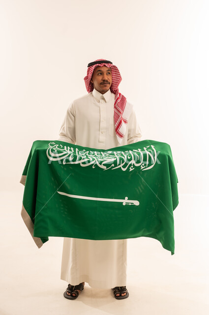 رجل سعودي بالزي التقليدي يمسك علم السعودية