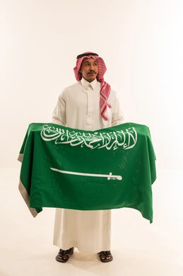 رجل سعودي بالزي التقليدي يمسك علم السعودية