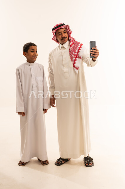 رجل وطفل سعودي يلتقطان صورة سيلفي بخلفية بيضاء