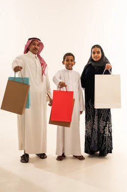 عائلة سعودية مع أكياس تسوق على خلفية بيضاء