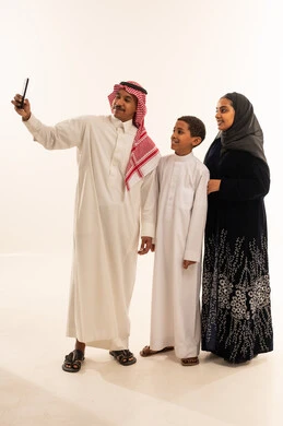 عائلة سعودية تلتقط صورة سيلفي بالهاتف على خلفية بيضاء