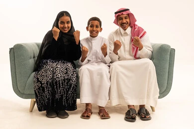 عائلة سعودية بالزي التقليدي تحتفل على الأريكة