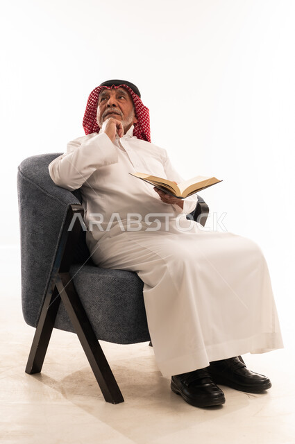 رجل سعودي مسن يقرأ كتاباً على كرسي