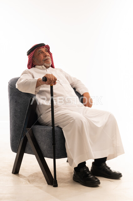 رجل سعودي مسن جالس على كرسي يحمل عصا