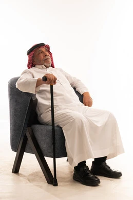 رجل سعودي مسن جالس على كرسي يحمل عصا