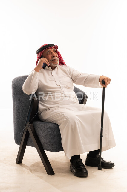 رجل سعودي مسن يتحدث بالهاتف مع عصا مشي