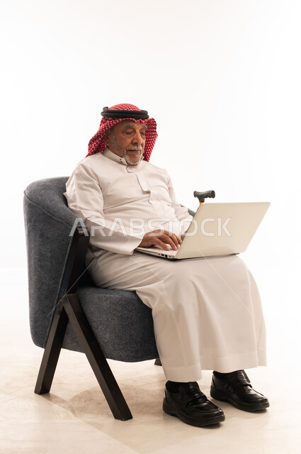 رجل سعودي مسن يستخدم الكمبيوتر المحمول جالساً على كرسي