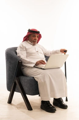Elderly Saudi Man Using Laptop in Blue Armchair White Background