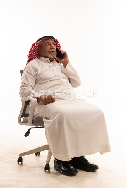 رجل سعودي مسن يتحدث بالهاتف على كرسي مكتب