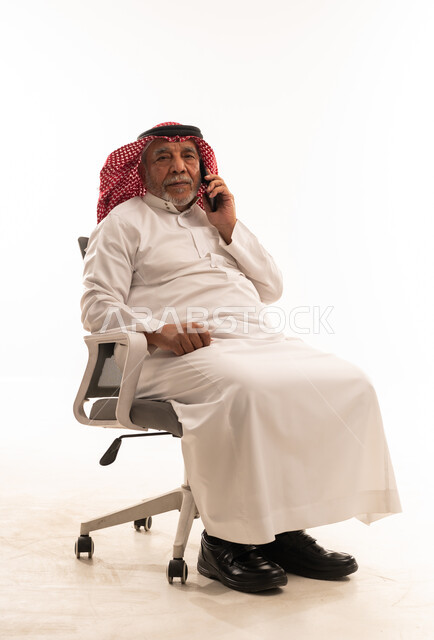 رجل سعودي مسن يتحدث بالهاتف على كرسي مكتب