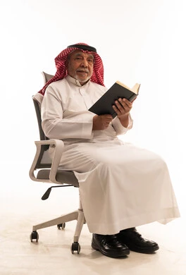 رجل سعودي مسن يقرأ كتاباً على كرسي مكتب