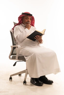رجل سعودي مسن يقرأ كتاباً على كرسي مكتب