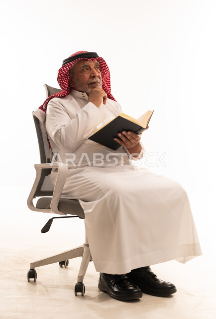 رجل سعودي مسن يفكر مع كتاب على كرسي مكتب