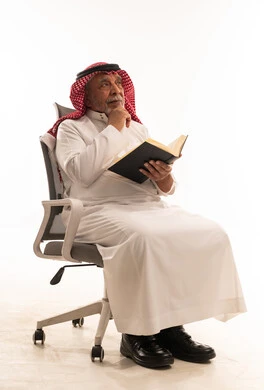 رجل سعودي مسن يفكر مع كتاب على كرسي مكتب