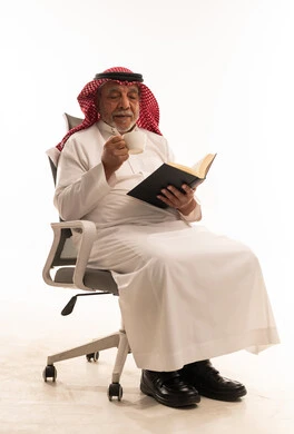 رجل سعودي مسن يقرأ كتاباً مع القهوة
