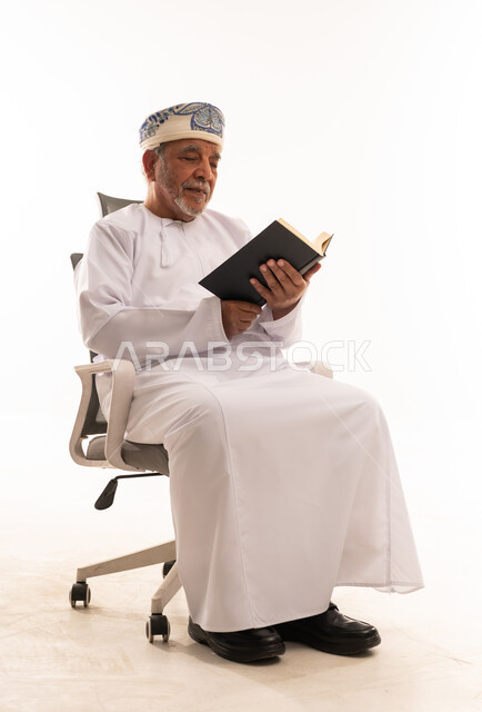 رجل عماني مسن يقرأ كتاباً على كرسي مكتب