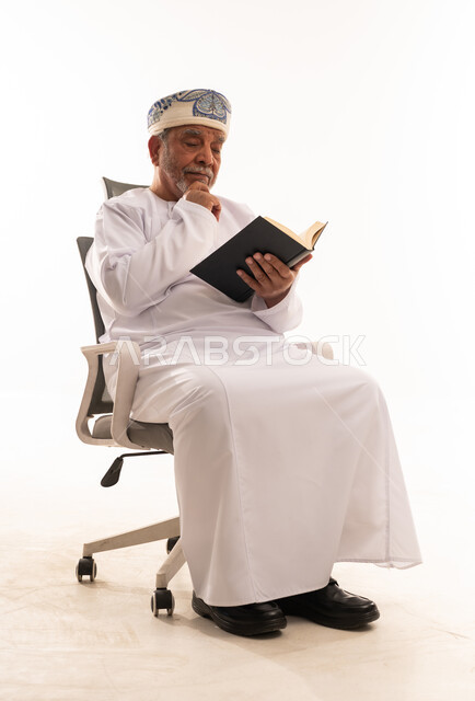 رجل عماني مسن يقرأ كتاباً في الاستوديو