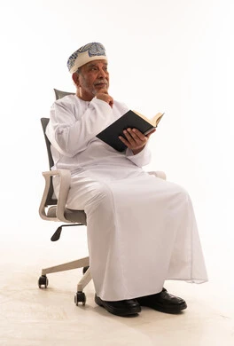 Elderly Omani Man in Traditional Dress Reading a Book