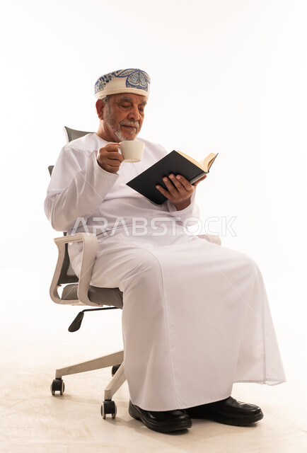 رجل عماني مسن يقرأ كتاباً مع القهوة