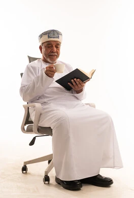 رجل عماني مسن يقرأ كتاباً مع قهوة