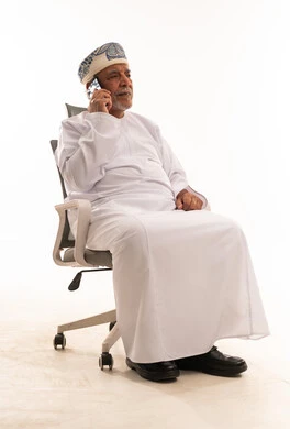 رجل عُماني مسن يتحدث بالهاتف على كرسي مكتب