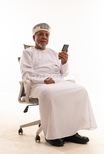 رجل عماني مسن بالزي التقليدي يستخدم الهاتف الذكي