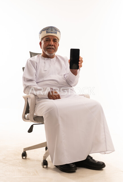 رجل عُماني مسن يمسك هاتف ذكي بخلفية بيضاء