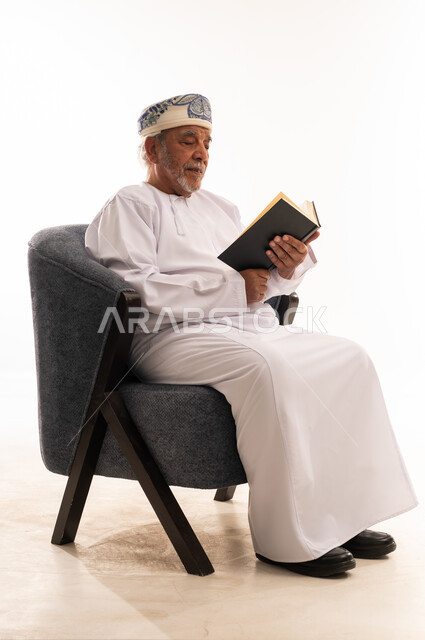 Elderly Omani Man Reading Book in Traditional Dress