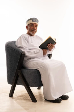 رجل عماني مسن يقرأ كتاباً على كرسي