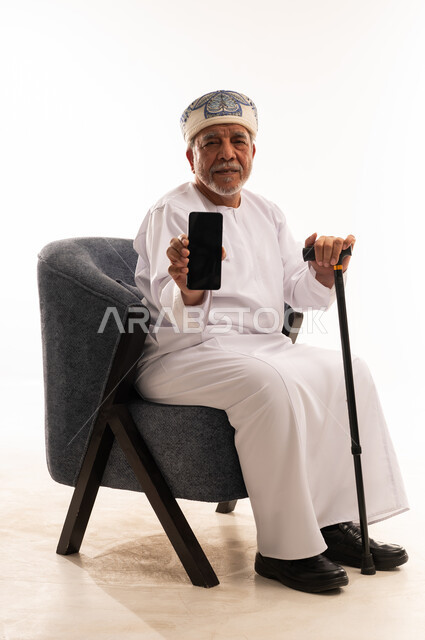 رجل عُماني مسن يمسك بهاتف ذكي وعصا مشي
