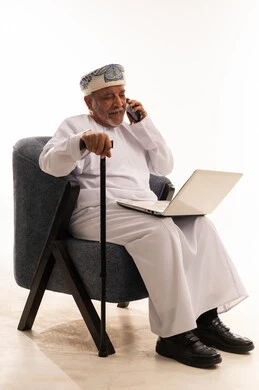Elderly Omani Man Using Laptop and Phone on White Background