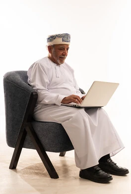 رجل عماني مسن يستخدم الحاسوب باللباس التقليدي