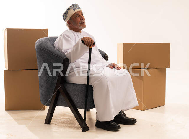 رجل عماني مسن يجلس مع صناديق وعصا مشي