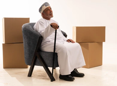 رجل عماني مسن يجلس مع صناديق وعصا مشي