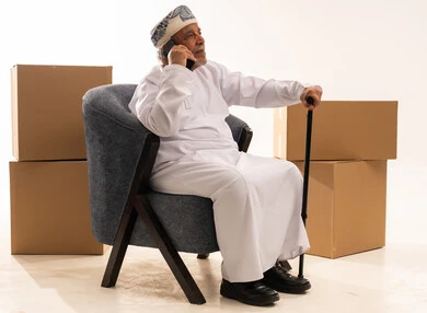 رجل عماني مسن يتحدث بالهاتف مع صناديق شحن