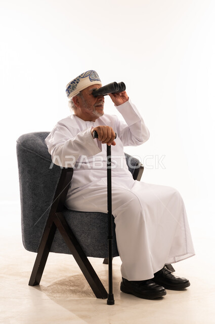 رجل عماني مسن يستخدم منظار وعصا مشي