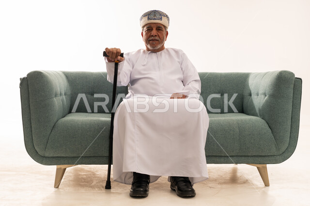 رجل عماني مسن يجلس على أريكة مع عصا