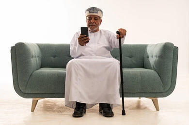 Elderly Omani Man Using Smartphone on Sofa