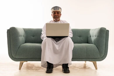 رجل عماني مسن يستخدم المحمول على الأريكة