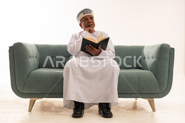 Elderly Omani Man Reading Book on Sofa