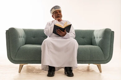 Elderly Omani Man Reading Book on Sofa