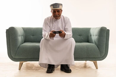 رجل عماني مسن يلعب ألعاب الفيديو على الأريكة