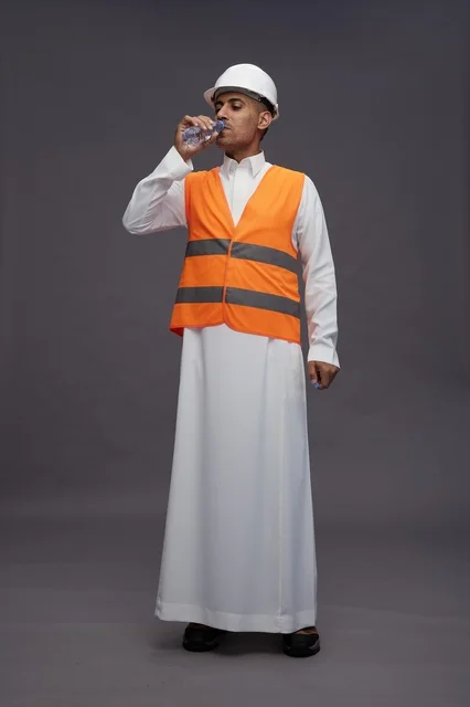 عامل سعودي بمعدات السلامة يشرب الماء في الاستوديو