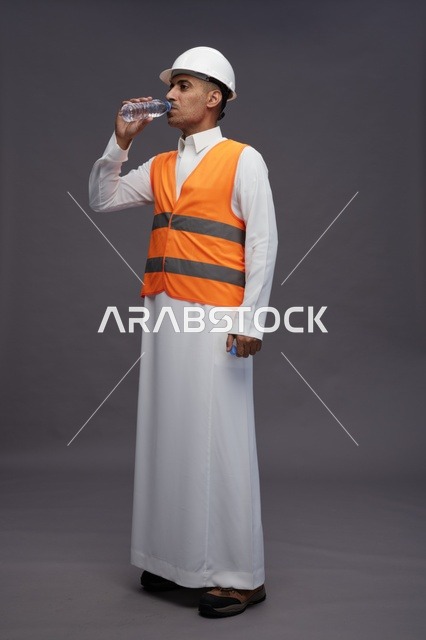 عامل سعودي يرتدي سترة السلامة يشرب الماء في الاستوديو