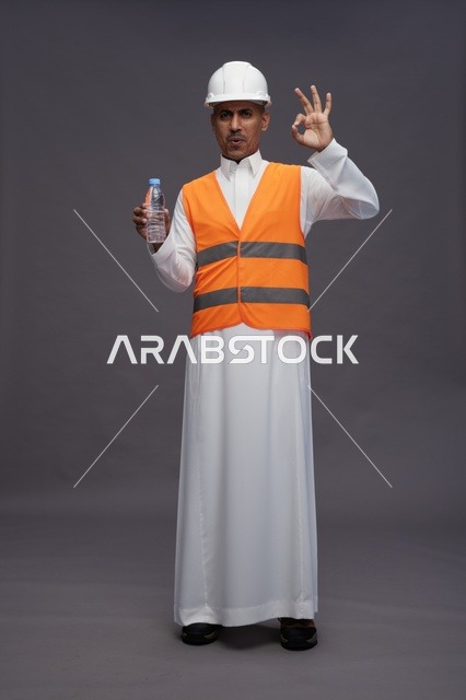 عامل سعودي يرتدي معدات السلامة ويحمل زجاجة مياه في الاستوديو