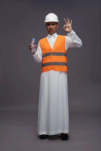 عامل سعودي يرتدي معدات السلامة ويحمل زجاجة مياه في الاستوديو