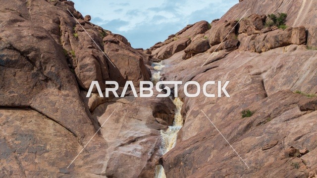 شلال في جبل صحراوي يتدفق عبر وادي صخري في حائل