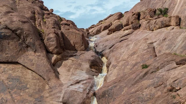 A waterfall in a desert mountain flowing through a rocky valley in Hail.